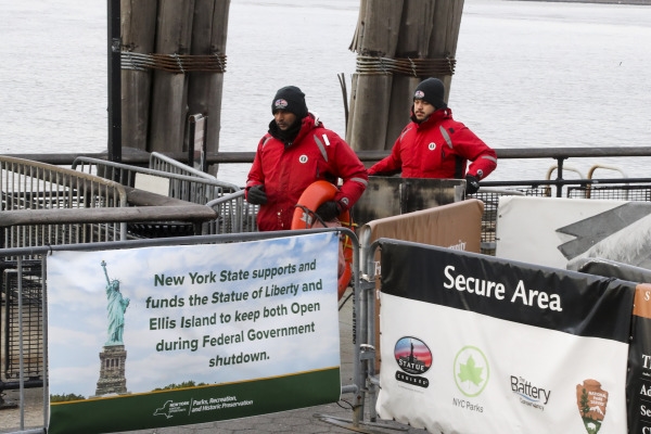 12日，在纽约的去往自由女神像的码头，工人身边的告示上写着由于联邦政府部分停摆，纽约州政府资助其继续开放。新华社图